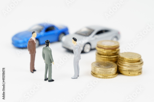 Three miniature figures of a businessman, coins and cars in the background.