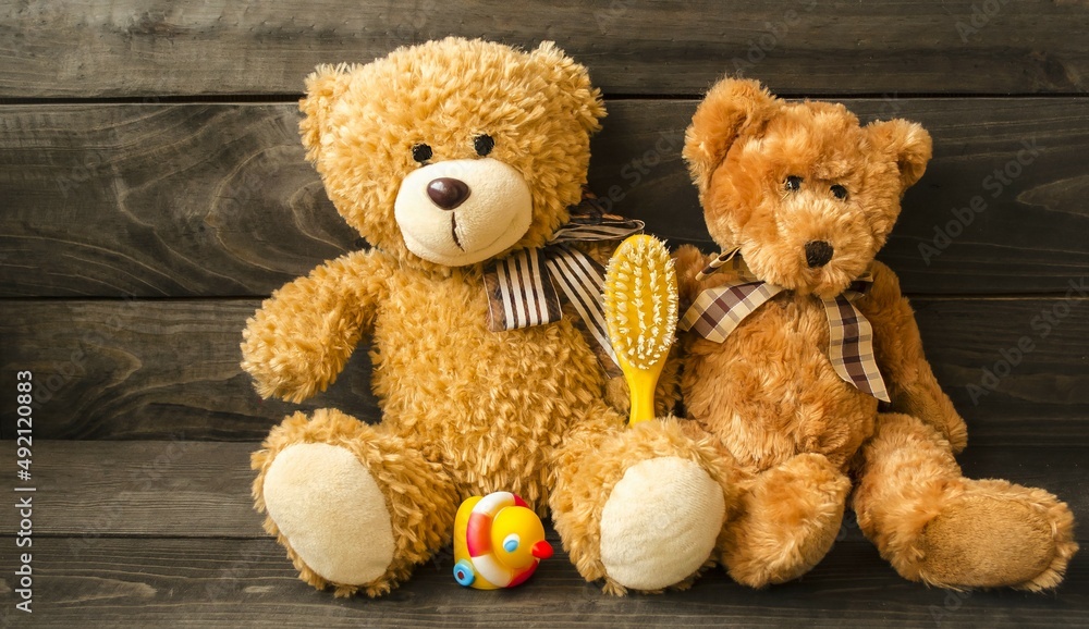 Obraz premium Fluffy teddy bears sit on a wooden table with a children's comb and a small rubber duck. The concept of children's hygiene and cleanliness. Banner, decorative card, background image, close-up front 