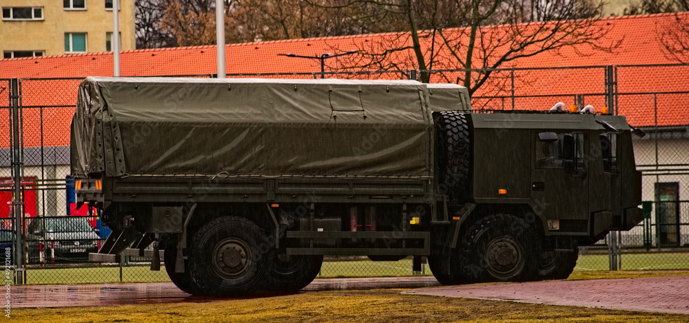 Wojskowe ciężarówki w kolorze khaki zaparkowane na placu ogrodzonym siatką stalową w czasie deszczu . Military trucks in Khaki color parked on a square fenced steel grid during rain.  - obrazy, fototapety, plakaty 