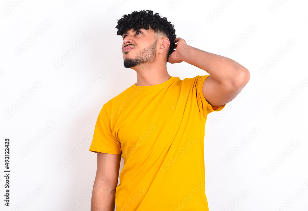young arab man wearing yellow T-shirt over white background confuse and wonder about question. Uncertain with doubt, thinking with hand on head. Pensive concept. young arab man wearing yellow T-shirt over white background confuse and wonder about question. Uncertain with doubt, thinking with hand on head. Pensive concept.