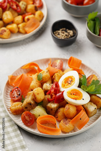 Sweet potato gnocchi with teriyaki tofu with indonesian vegetable salad gado gado - carrots, cucumbers, tomatoes, coriander, sesame seeds, boiled eggs and peanut butter dressing on a white plate