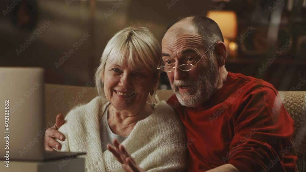 Glad elderly man embracing smiling wife and talking with relatives while making video call via netbook at home Glad elderly man embracing smiling wife and talking with relatives while making video call via netbook at home