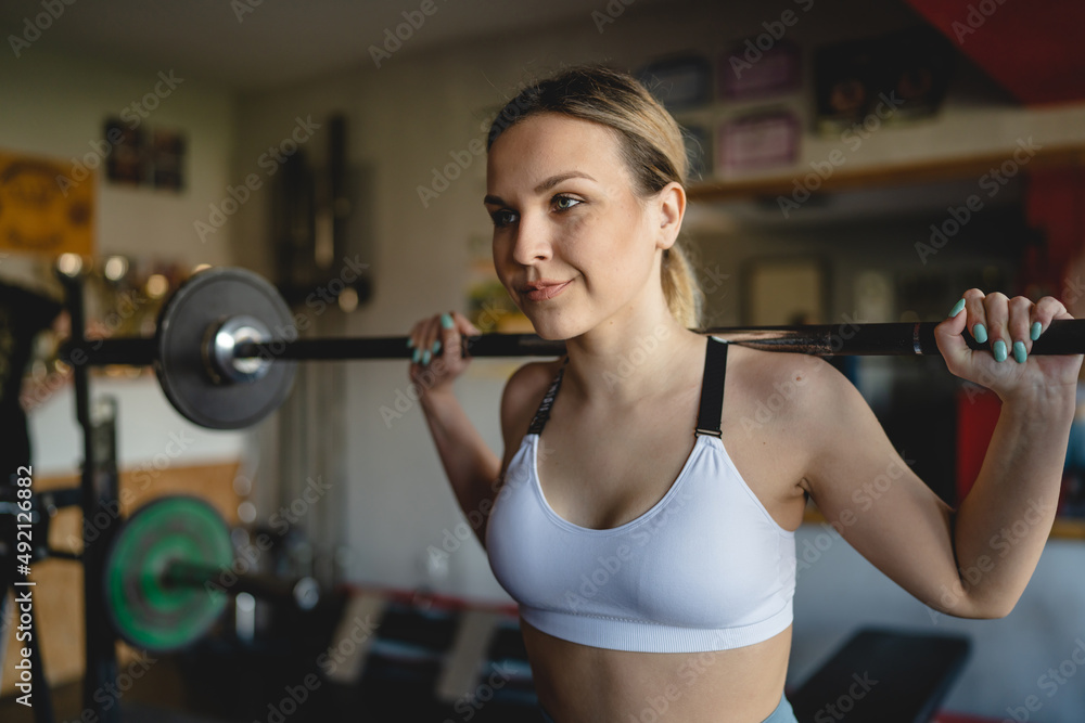 Obraz premium One woman training at gym female athlete doing squats with barbell and weight on her shoulders close up copy space strength and fitness exercise concept