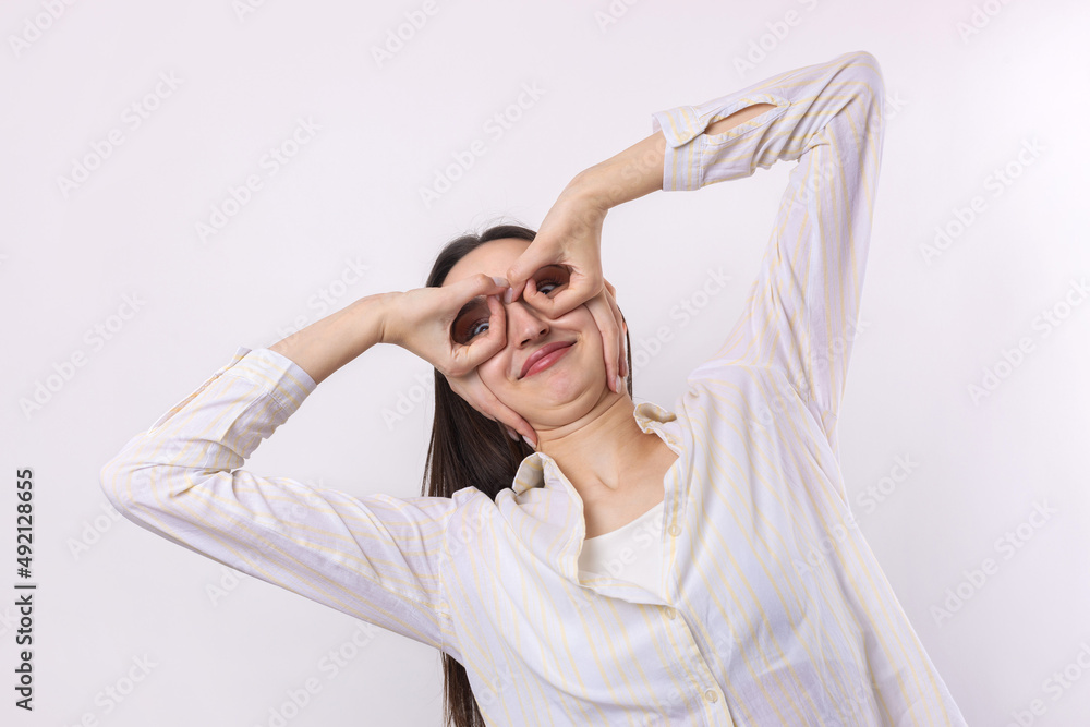 Close up portrait of attractive quirky young woman making binoculars with hands showing ok gesture on white studio background. Close up portrait of attractive quirky young woman making binoculars with hands showing ok gesture on white studio background.