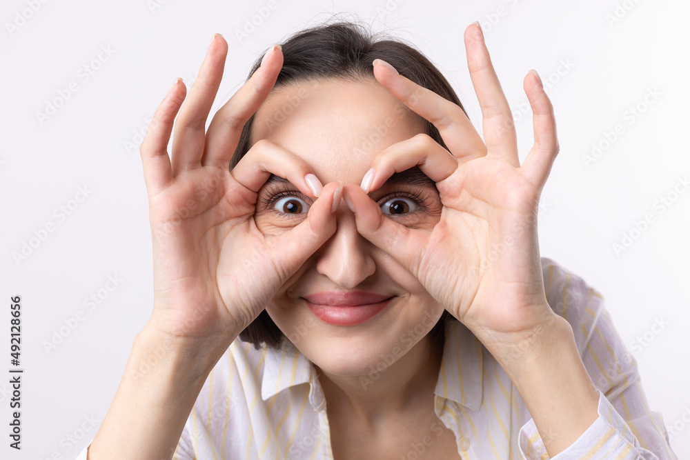 Close up portrait of attractive quirky young woman making binoculars with hands showing ok gesture on white studio background. Close up portrait of attractive quirky young woman making binoculars with hands showing ok gesture on white studio background.