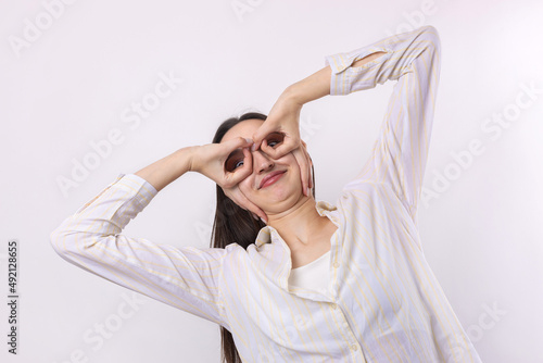 Close up portrait of attractive quirky young woman making binoculars with hands showing ok gesture on white studio background.