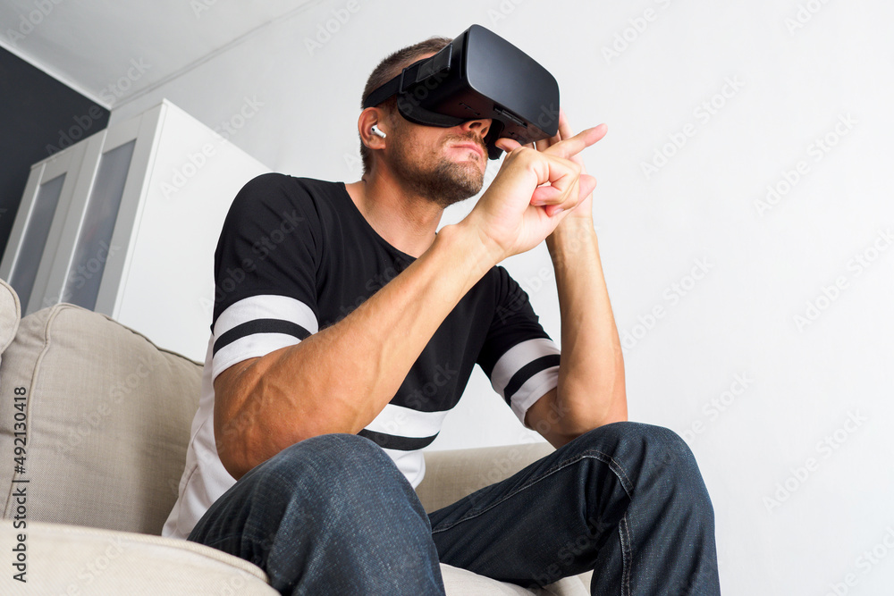 Man using virtual reality simulator headset, sitting on couch at home.