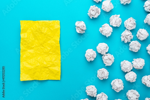 Top view of new idea concept over turquoise blue background. Great business idea concept with white crumpled office paper and yellow paper. Business plan on yellow crumpled paper after brainstorming.