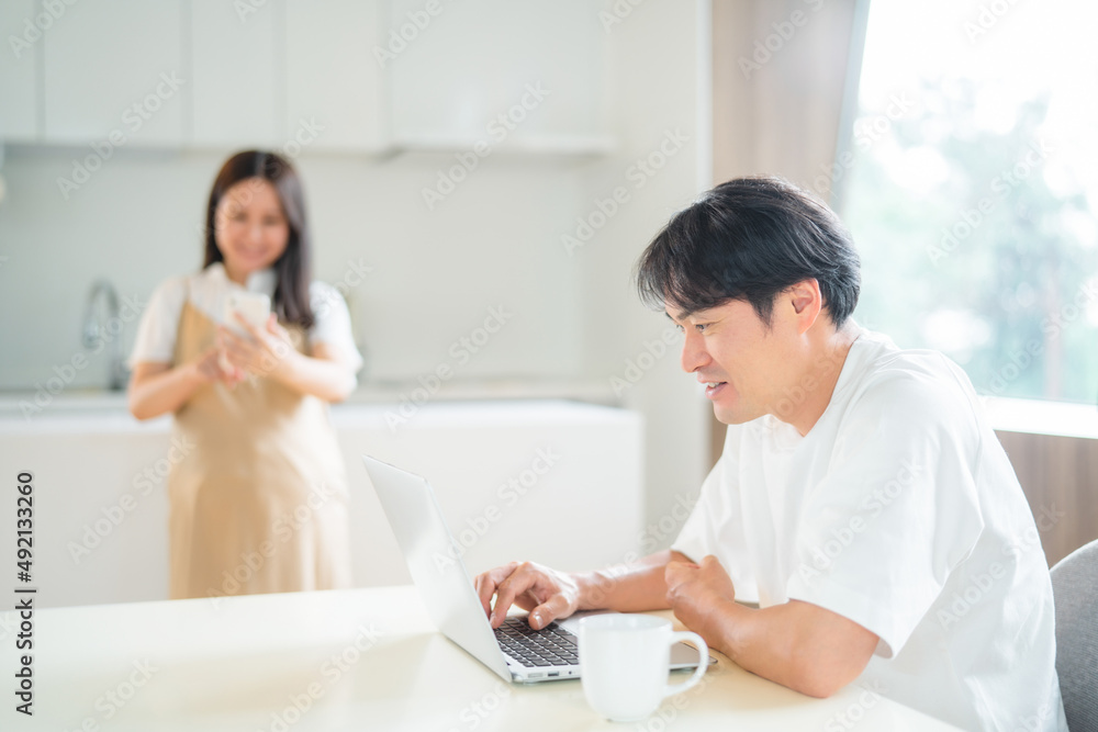 テレワークする男性とスマホを使う妊婦(笑顔)
テレワークする男性とスマホを使う妊婦(笑顔)