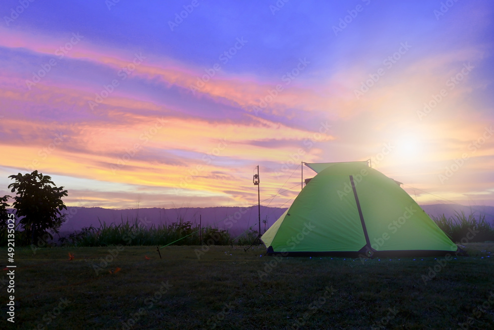 orange tent glows in the tent yard under the dramatic evening sky, the sun is setting red-orange-purple. mountain scenery in summer landscape background