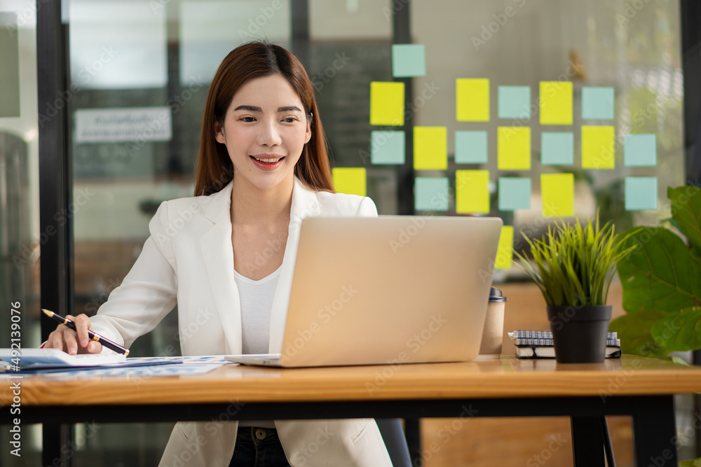 Pretty Asian woman working and typing on a laptop computer at the office. businesswoman looking at financial statistics data analysis chart graph profit growth business idea Pretty Asian woman working and typing on a laptop computer at the office. businesswoman looking at financial statistics data analysis chart graph profit growth business idea