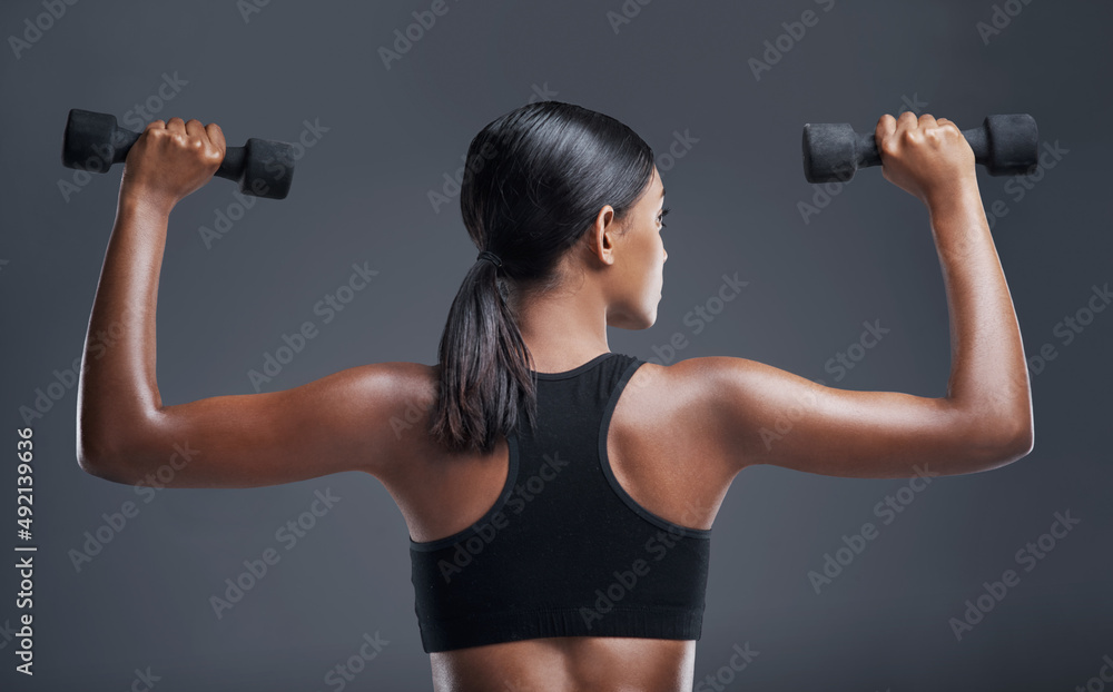 The body you want is earned through determination. Studio shot of a sporty young woman lifting weights against a grey background. The body you want is earned through determination. Studio shot of a sporty young woman lifting weights against a grey background.