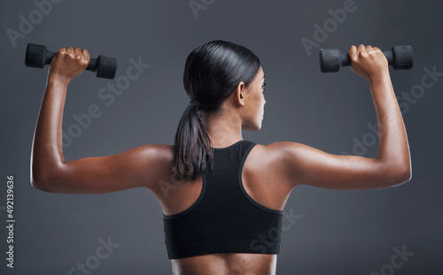 The body you want is earned through determination. Studio shot of a sporty young woman lifting weights against a grey background. © Angelo J/peopleimages.com