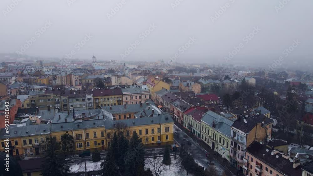 Sad gloomy city with foggy sky. Wet snow is falling from sky. Bright houses along gray streets. Church with domes. Winter. Cold weather. View from quadcopter Sad gloomy city with foggy sky. Wet snow is falling from sky. Bright houses along gray streets. Church with domes. Winter. Cold weather. View from quadcopter
