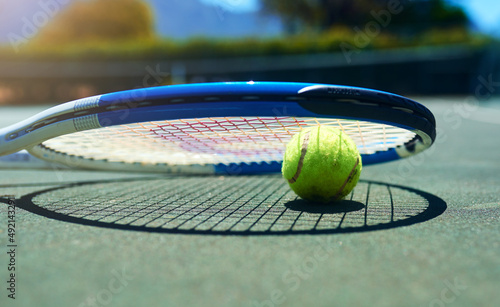 Its the perfect day for a tennis game. Cropped shot of a tennis racket and ball on an empty court during the day.