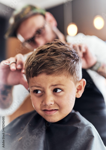 This hairstyle is looking cooler by the minute. Cropped shot an adorable little boy getting a haircut at the barbershop.