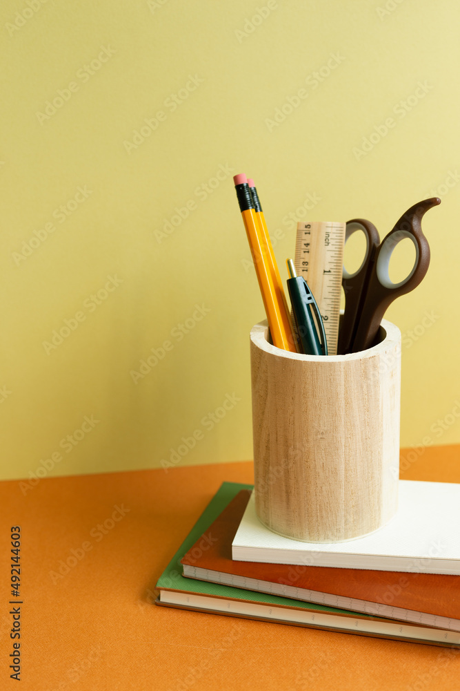 Notebook and pencil holder on orange desk. yellow wall background. workspace