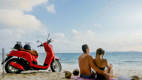 Scooter road trip. Lovely couple on red motorbike in white clothes on sand beach. Just married people kiss hugs walking near the tropical palm trees, sea. Wedding honeymoon by ocean. Motorcycle rent.