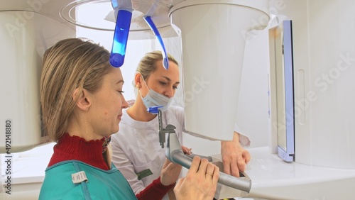 Doctor to take a image 3d scanner tomography of teeth and jaw in modern laboratory dental clinic. Female nurse shows the patient woman an x-ray machine 3d digital scanner. Computer dental diagnostics.