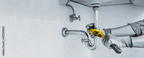 Photography Technician plumber using a wrench to repair a water pipe under the sink