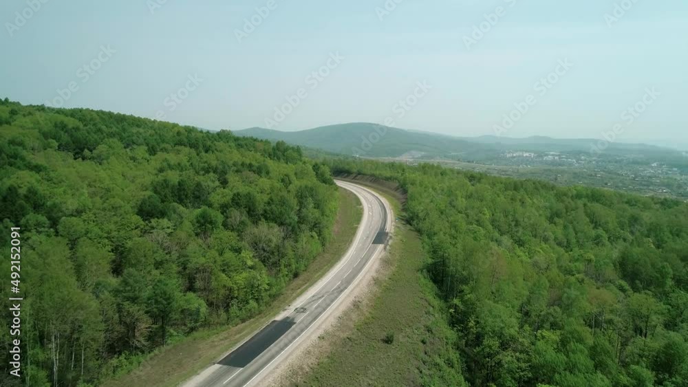 Aerial view of an asphalt intercity country road between green forest with a car driving on it Aerial view of an asphalt intercity country road between green forest with a car driving on it