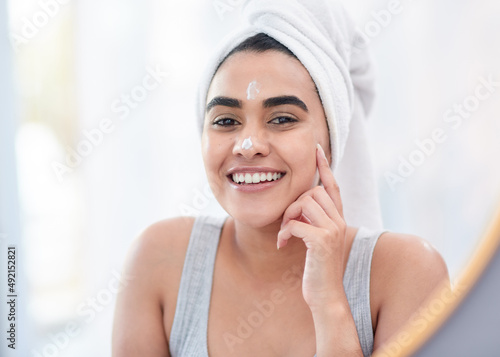 Start your day the fresh way. Shot of happy young woman applying facial moisturiser in front of her mirror.