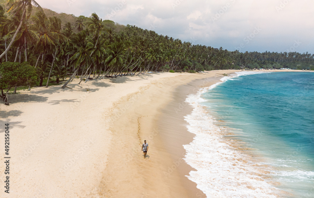 Podróżnik idący tropikalną plażą na tle palm i niebieskiego oceanu, piękny krajobraz.