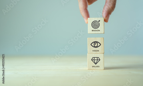 Mission, vision and values of company. Purpose business concept. Hand holds wooden cube with mission vision and values symbols on grey background. Modern vertical design. Business presentation. Banner photo
