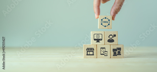 Omnichannel marketing concept. Digital online marketing commerce sale. For customer engagement by integrated online and offline channels. Hand holds wooden cube with omni text standing with omni icon photo