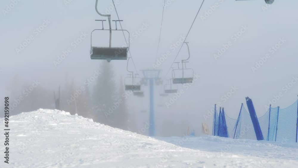 Empty chairlift moves up above the slopes at ski resort in snowing weather. Empty chairlift moves up above the slopes at ski resort in snowing weather.