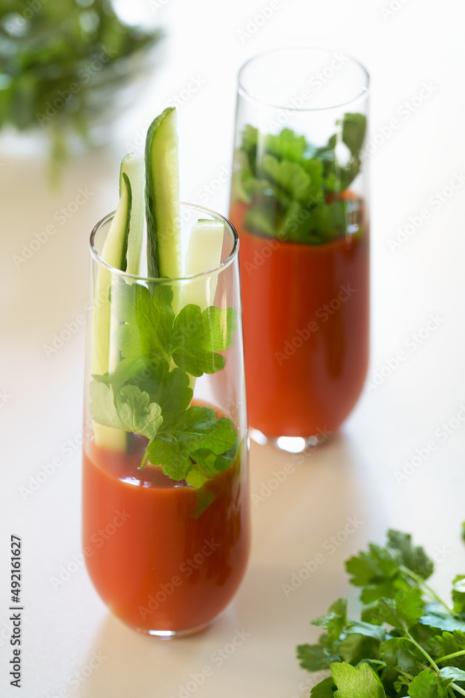 tomato juice with parsley and cucumber in glass glasses on a light background tomato juice with parsley and cucumber in glass glasses on a light background