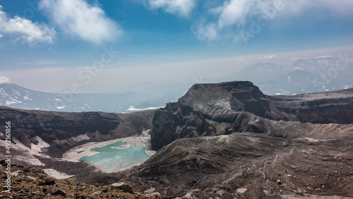 A lifeless acid lake on top of an active volcano. Snowmelt on the steep slopes of the crater and turquoise water. Rocky ground in the foreground. Kamchatka. Gorely Volcano photo