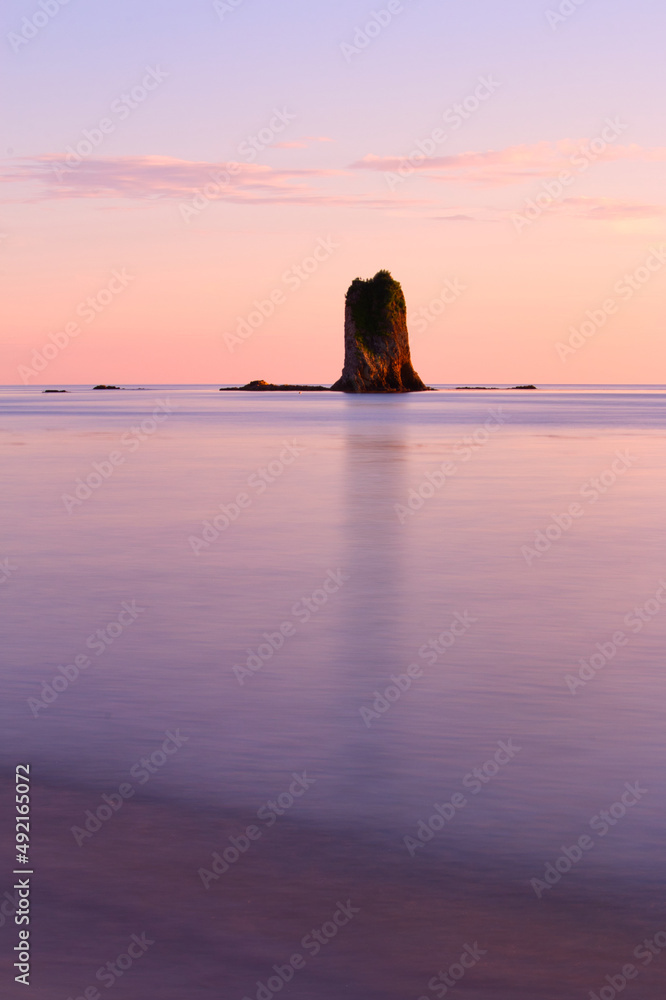 Pillar of rock reflected in flat wet purple sand at sunrise