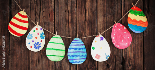 Paper Easter painted eggs painted hang on clothespins on background old wooden wall.