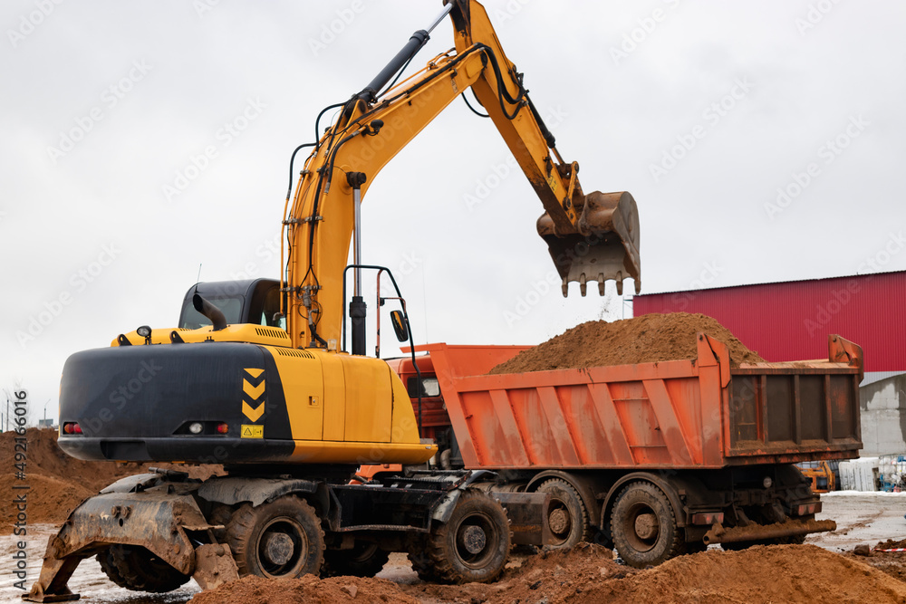 An excavator loads soil or sand into a dump truck. Pit development. Earthworks with the help of heavy construction equipment.