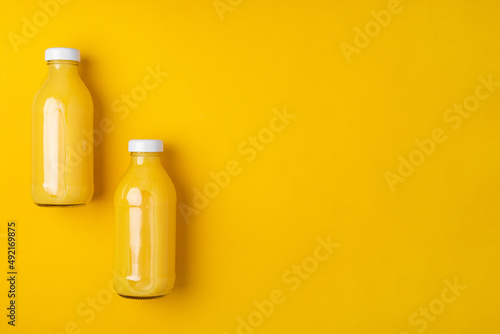 Two glass bottles with orange juice on a bright yellow background