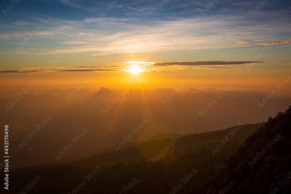 Mountains in clouds at sunrise in summer. Aerial view of mountain peak in fog. Beautiful landscape with high rocks, forest, sky. Top view from drone of mountain valley in low clouds. Foggy hills 