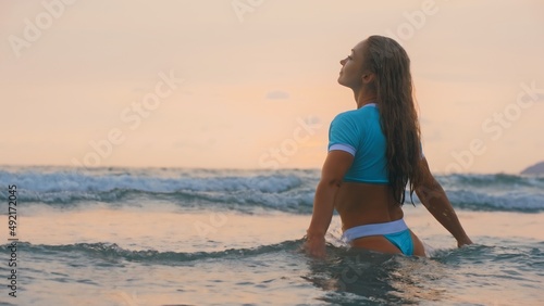 SLOW MOTION GLOW MIST DARK SILHOUETTE CINEMATIC VIEW: Sexy hot woman standing on water sea. Girl stand in turquoise swimsuit. Freedom paradise holiday vacation summer beach, seaside landscape concept