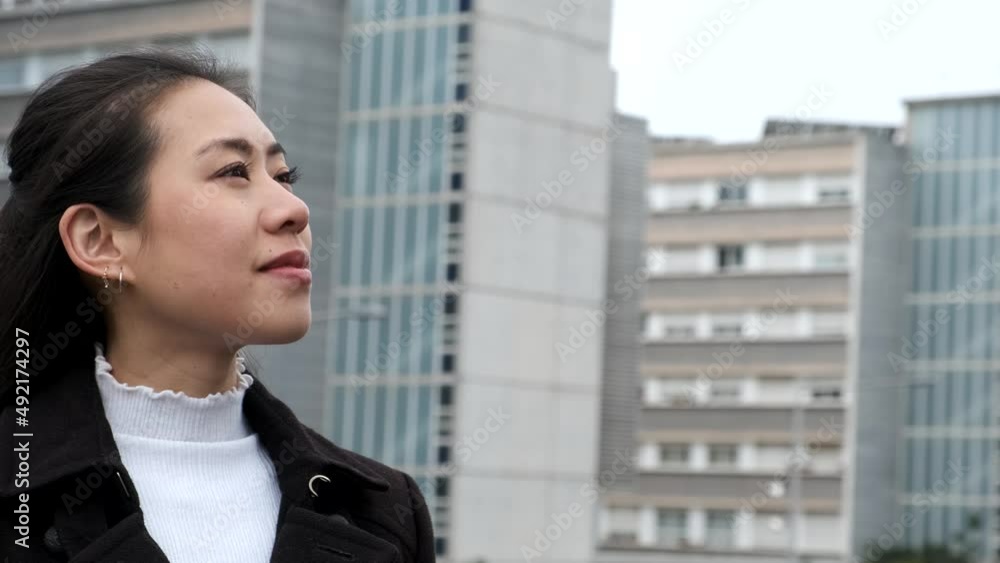 Pan around view of glad Chinese female entrepreneur smiling and looking away while standing against skyscrapers in downtown Pan around view of glad Chinese female entrepreneur smiling and looking away while standing against skyscrapers in downtown