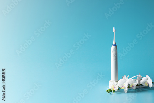 Modern ultrasonic toothbrush and white prchid flower on  blue gradient background.Copy space photo