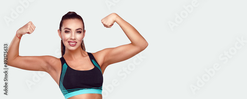 Smiling attractive caucasian fitness woman shows her perfect strong muscles body on gray isolated background © khmelev