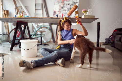 A young female artist is sitting on the floor with her dog while taking a small break from working on a new painting in the studio. Art, painting, friendship, studio