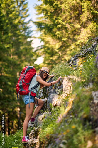 Caucasian hiker woman climbing cliff in forest. Backpacker girl in casual clothes. Hiking, lifestyle, nature concept