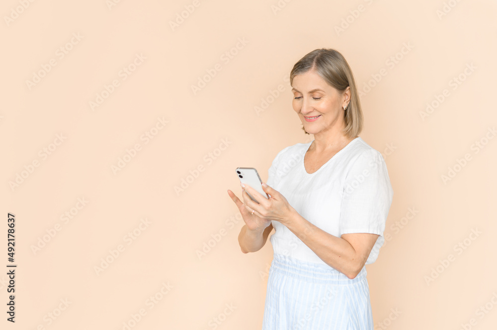Old attractive woman use smartphone on a beige background. Isolated portrait in light clothes. Old attractive woman use smartphone on a beige background. Isolated portrait in light clothes.