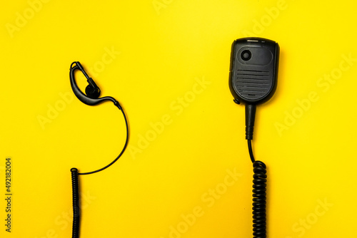 Black broadcast microphone and one ear headphones on yellow background with side space. A close up image of a walkie-talkie set along with its set of headphones.