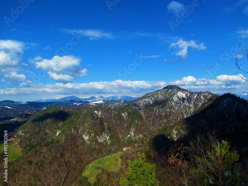 Scenic view of mountain Tosc in the hills of Polhov Gradec, Slovenia and snow covered peaks of Julian alps in the background photo