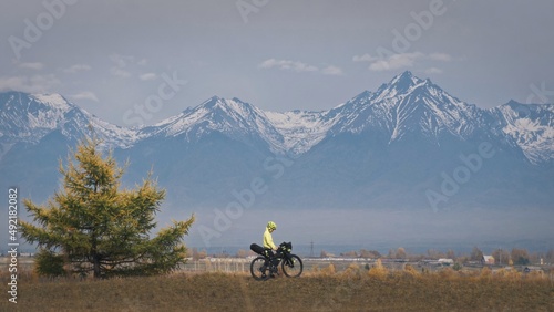 The woman travel on mixed terrain cycle touring with bikepacking. The traveler journey with bicycle bags. Sport tourism bikepacking, bike, sportswear in green black colors. Mountain snow capped. photo