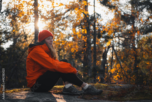 beautiful brunette traveller is sitting on top of a hill on a rock, resting after a hard climb. Sunset on top of a mountain in Vuokatti, Kainuu region, Finland. Natural smile of a girl in her 20s photo