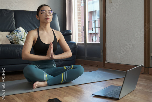Young asian woman listening relaxing music and meditating doing the easy pose (Sukhasana) at home.