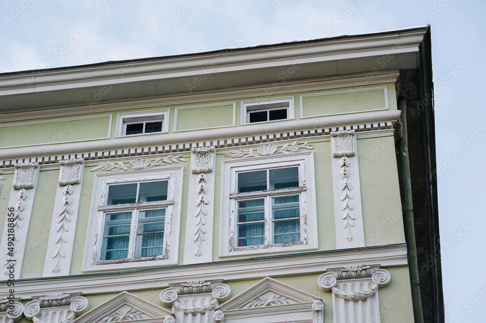 Two windows on the green facade of a neoclassical building with small white columns and capitals and decorative gypsum floral elements. Lviv, Ukraine.
